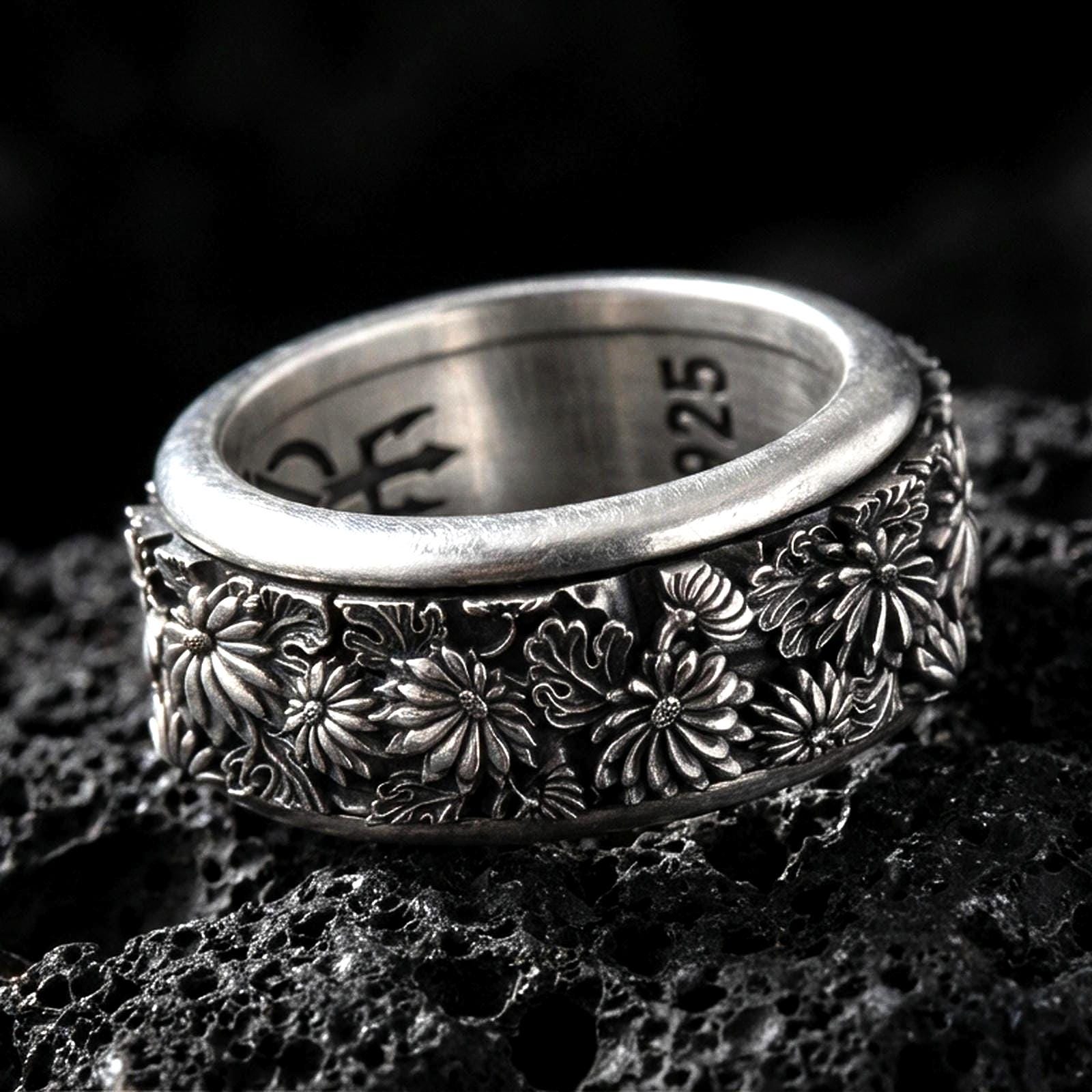 Sterling silver floral spinner ring photographed on volcanic rock with oxidized contrast highlighting the daisy blossoms and engraved petals.