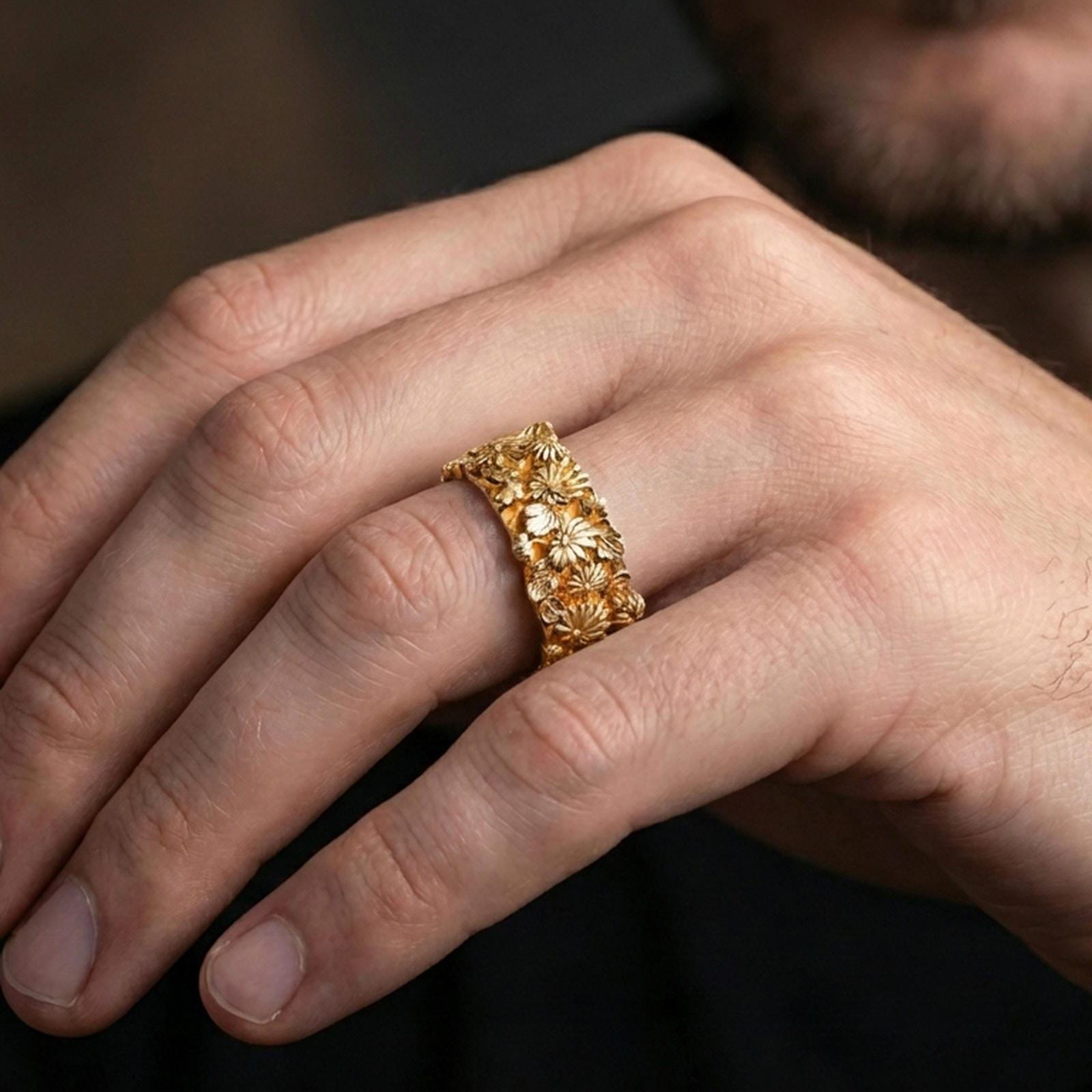 Gold plated floral band ring worn on a finger, warm reflective finish highlighting the raised blossoms and leaf detailing.