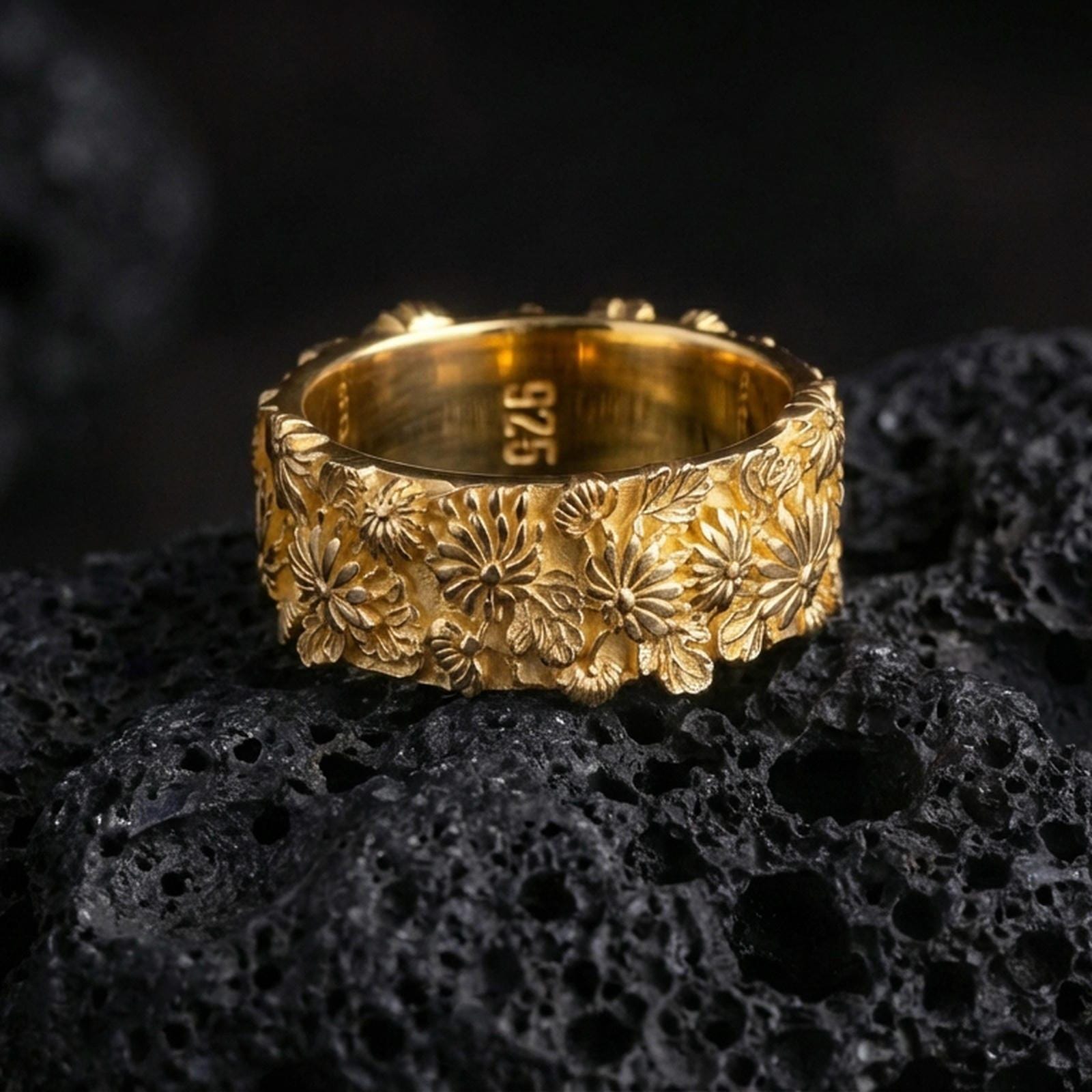 Floral relief ring displayed on volcanic rock with a gold plated finish, emphasizing the layered petals and sculpted leaves.