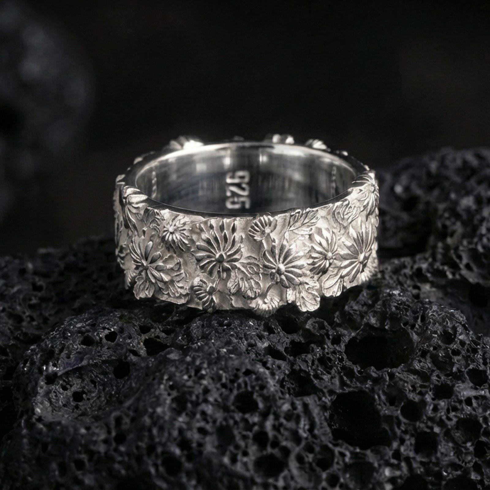 925 silver flower ring on black volcanic stone, polished silver edges framing the detailed blossom and foliage carving.