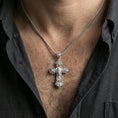 Load image into Gallery viewer, Polished silver floral cross pendant with masked portrait worn on the neck in a close lifestyle frame, highlighting the pendant against the chest
