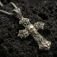 Load image into Gallery viewer, Bronze Chicano tattoo style cross pendant with rose details and masked face motif displayed on dark volcanic rock in a close-up luxury jewelry shot
