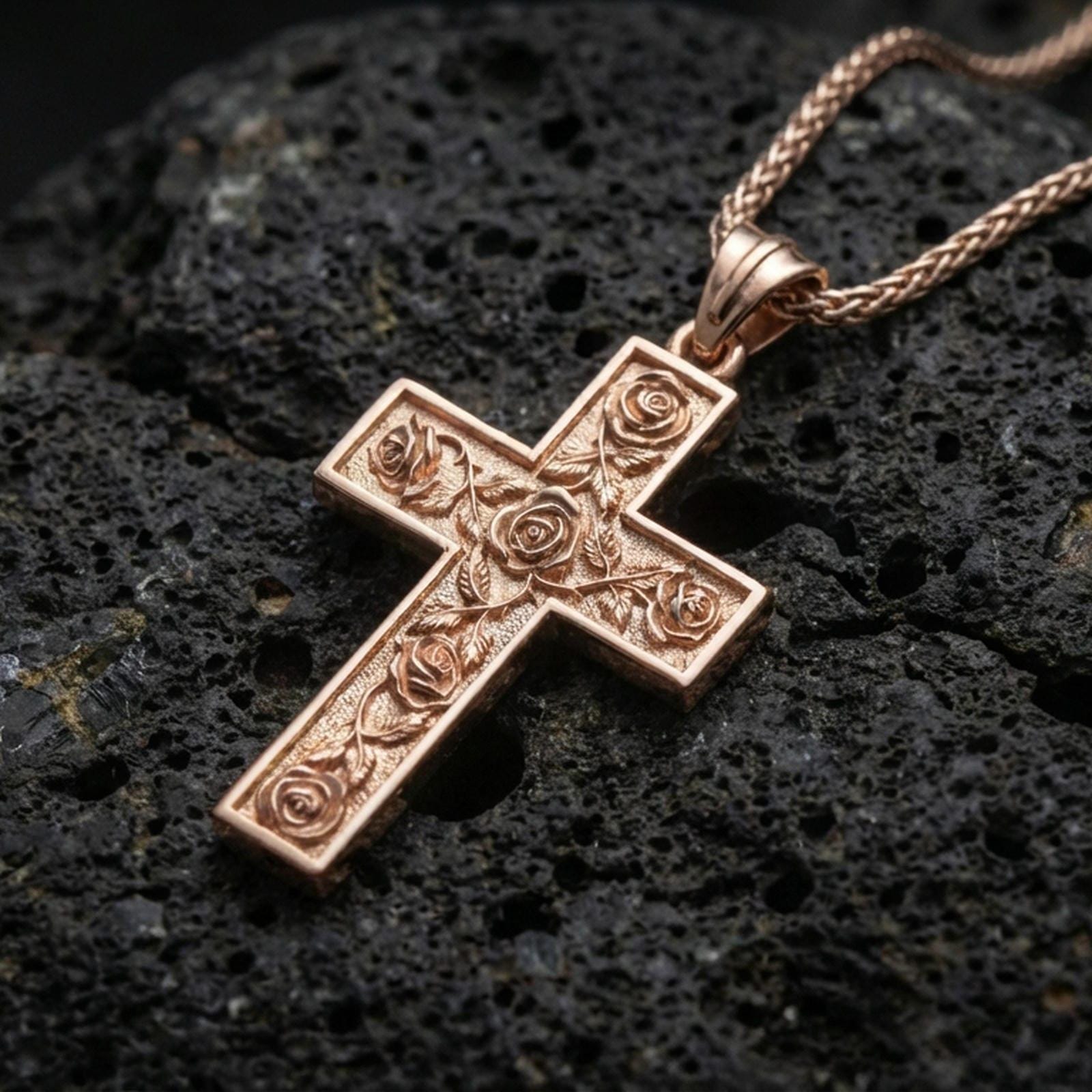 Rose gold plated Christian cross pendant with detailed rose accents resting on volcanic rock in an elegant close-up product presentation