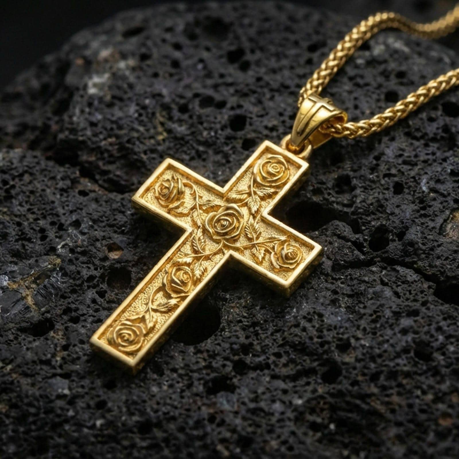Gold plated floral cross pendant with engraved rose vine details showcased on black volcanic rock in a refined macro jewelry image