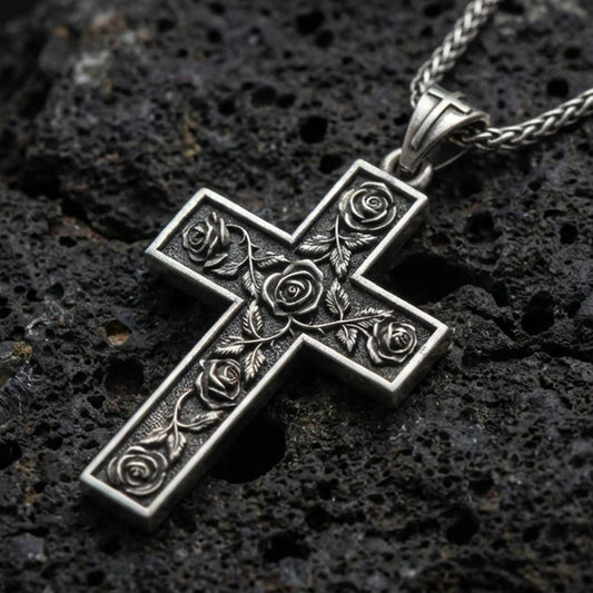 Oxidized rose cross pendant with engraved floral details displayed on dark volcanic rock in a close-up luxury jewelry composition