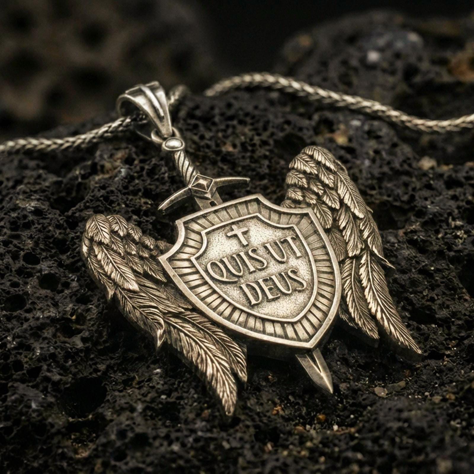 Bronze Saint Michael inspired shield pendant with angel wings, sword detail, and Quis Ut Deus inscription displayed on dark volcanic rock in a close-up luxury jewelry shot