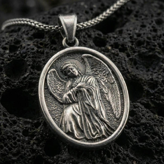 Oxidized angel pendant with oval frame and detailed winged figure displayed on dark volcanic rock in a close-up luxury jewelry composition