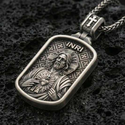 Oxidized Sacred Heart Jesus pendant with INRI detail and framed devotional portrait displayed on dark volcanic rock in a close-up luxury jewelry composition