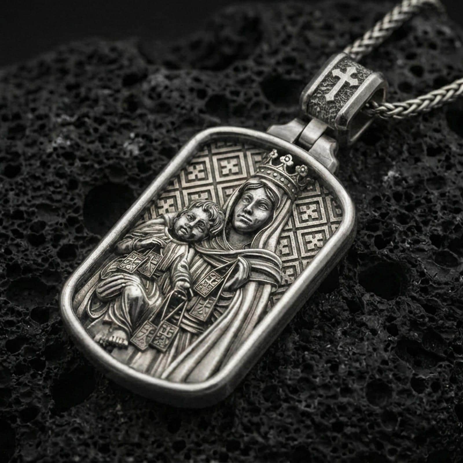 Oxidized Virgin Mary and Child pendant with crowned Madonna relief displayed on dark volcanic rock in a close-up luxury jewelry composition