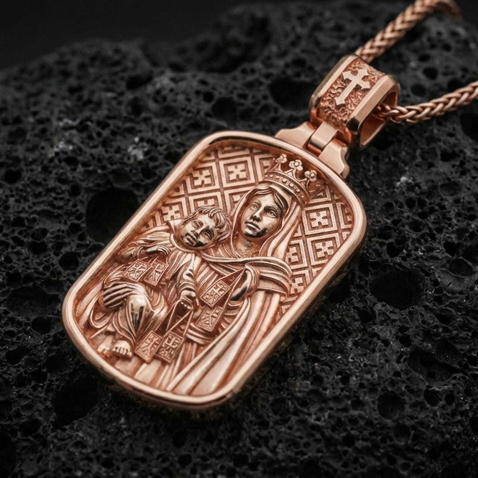 Rose gold plated Virgin Mary pendant with baby Jesus, crown detail, and framed icon design resting on volcanic rock in an elegant close-up product presentation