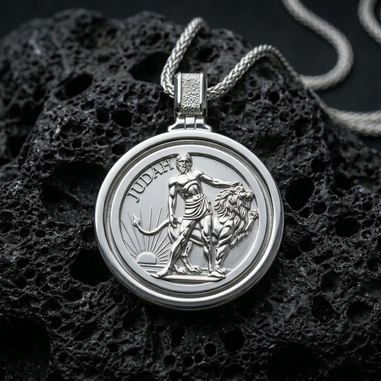 Polished silver Lion of Judah pendant with a round spinner-style frame, detailed lion relief, and sunrise motif placed on textured volcanic rock in a premium studio product shot