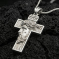 Load image into Gallery viewer, Polished silver Christian cross pendant with sculpted Jesus face, wood-textured cross relief, and INRI inscription placed on textured volcanic rock in a premium studio product shot
