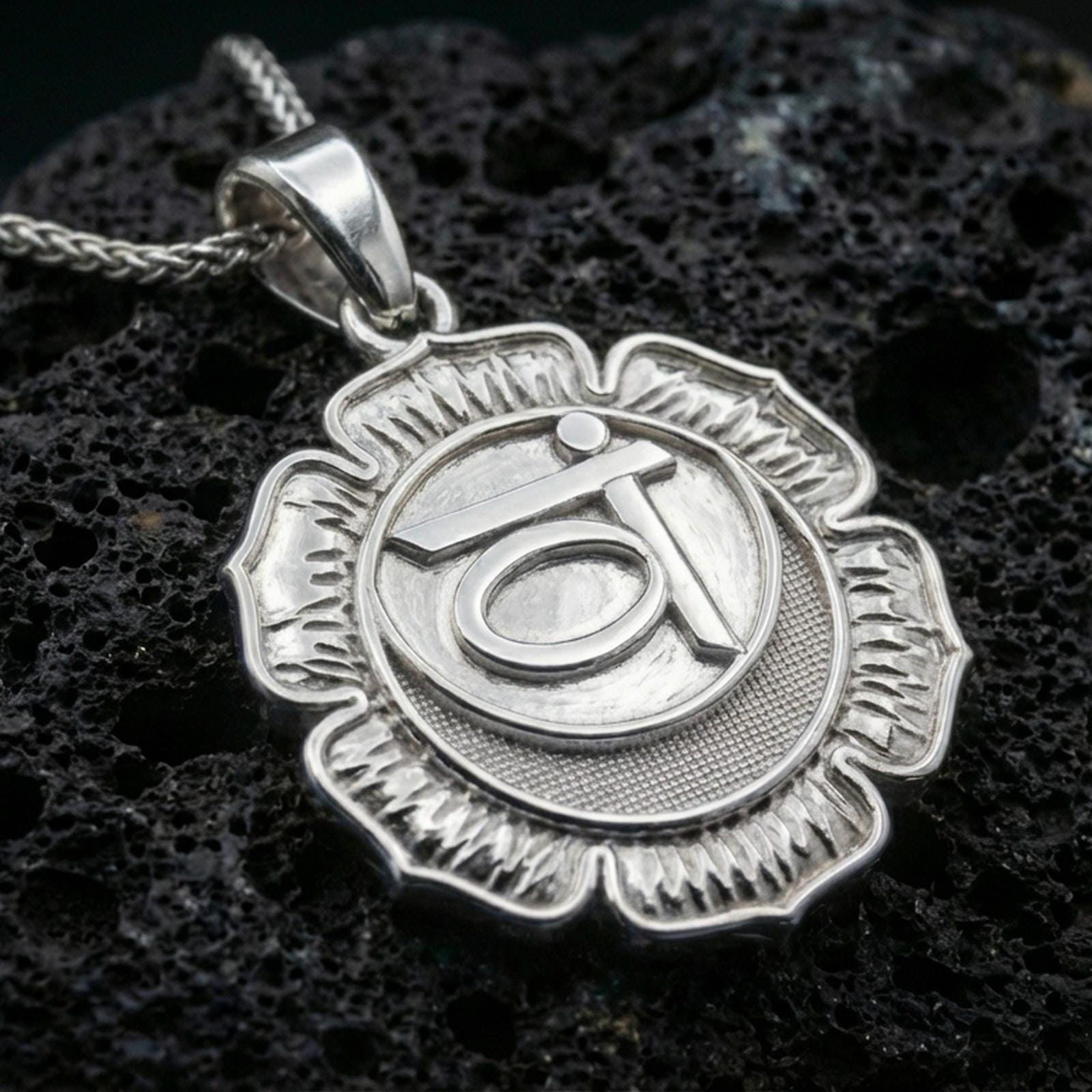 Polished silver chakra necklace with layered lotus design, circular center, and engraved throat chakra symbol placed on textured volcanic rock in a premium studio product shot