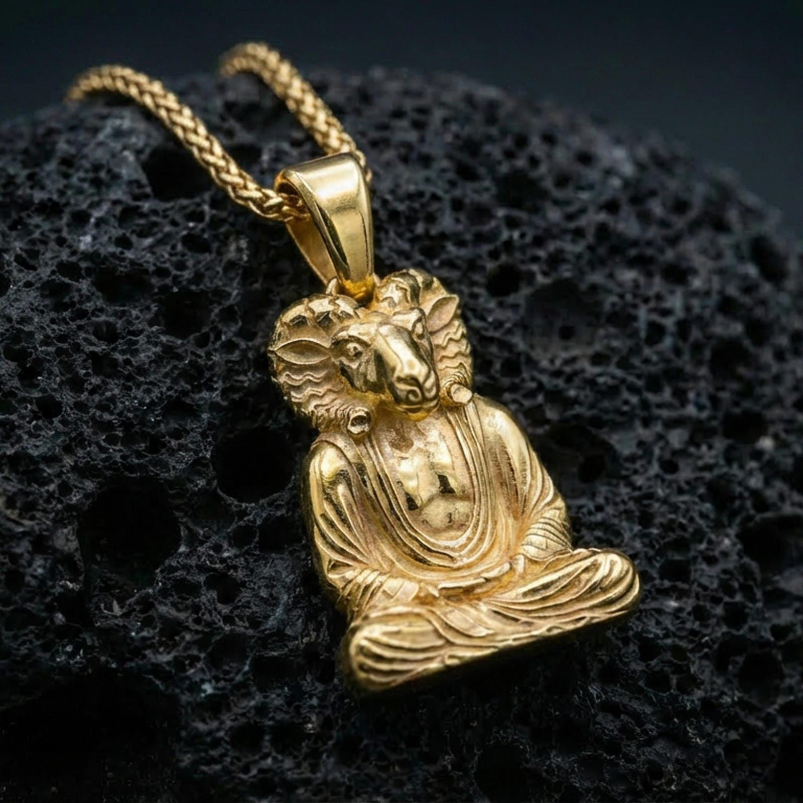 Sterling silver Khnum deity necklace pendant with a gold plated finish, seated ram-headed Egyptian god design with intricate relief, macro product shot on volcanic rock