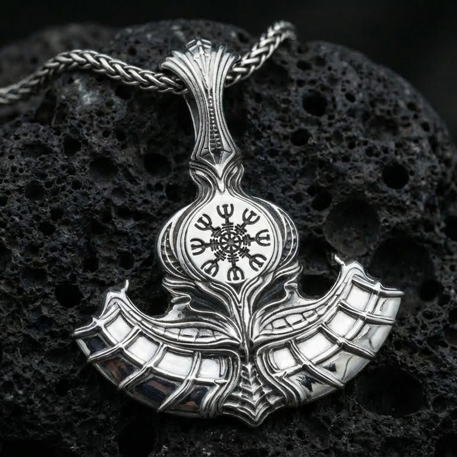 Sterling silver Norse axe necklace pendant in a polished silver finish, sculpted battle axe with Vegvisir runic compass emblem, macro product shot on volcanic stone