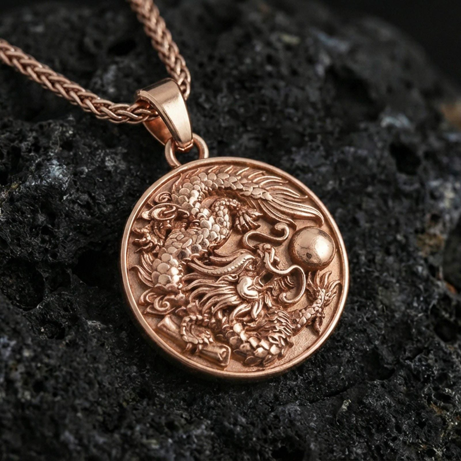 Sterling silver dragon medallion pendant with a rose gold plated finish, round high-relief dragon design with dramatic depth, macro on black volcanic rock