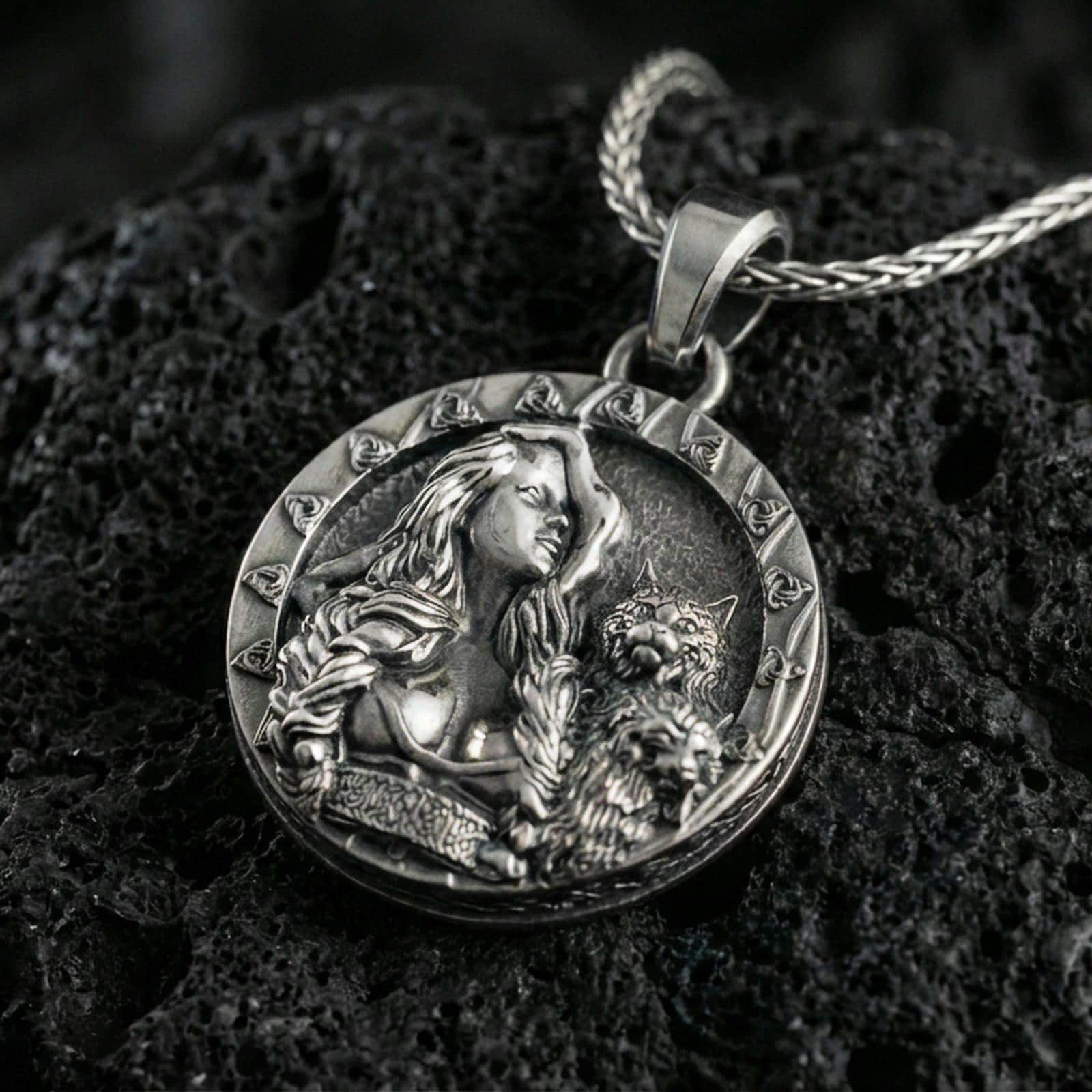 Sterling silver Freya goddess medallion pendant with an oxidized finish, Norse goddess portrait with cat companion relief, close-up on black volcanic rock