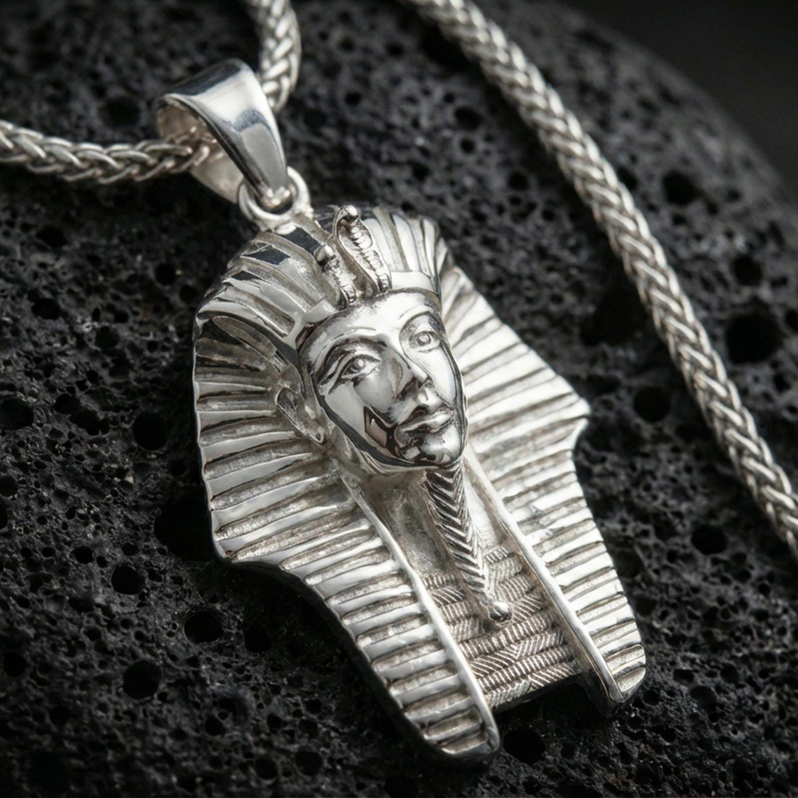 Sterling silver pharaoh head pendant in a polished silver finish, crisp carved headdress lines and facial details, macro on volcanic stone