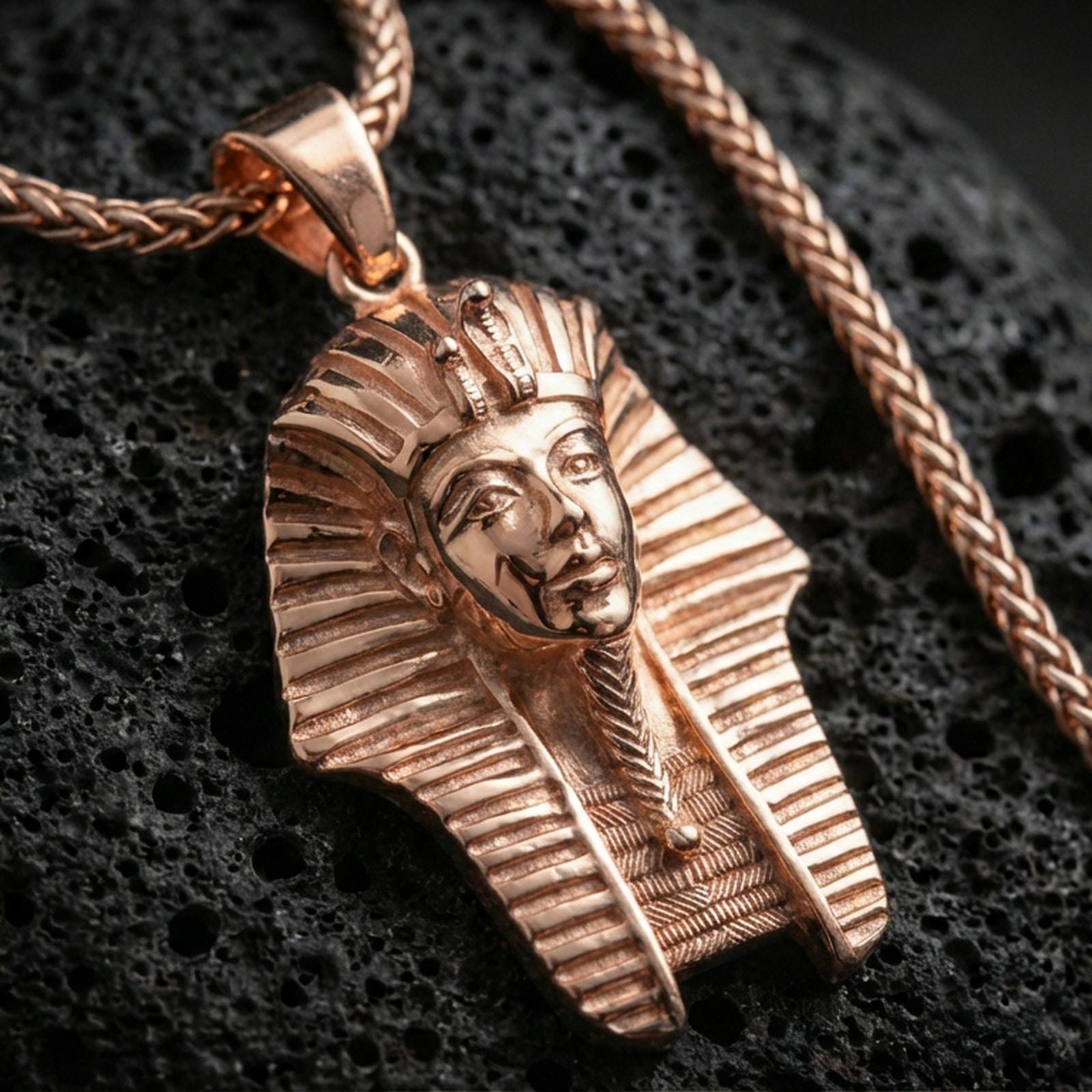 Sterling silver pharaoh head pendant with a rose gold plated finish, sculpted Egyptian pharaoh face and striped headdress, macro on black volcanic rock