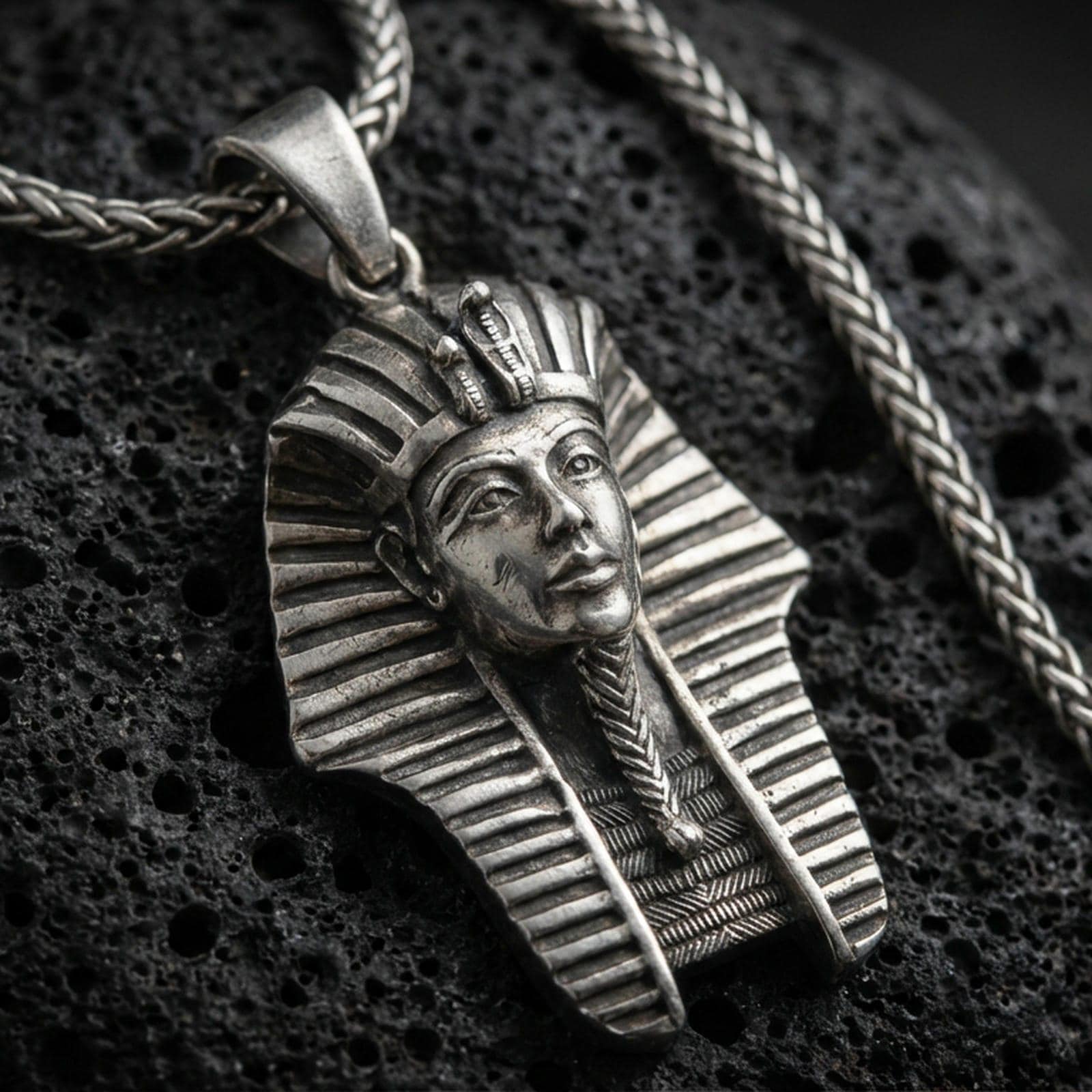 Sterling silver pharaoh head pendant with an oxidized finish, detailed Egyptian headdress and face relief, close-up on black volcanic rock