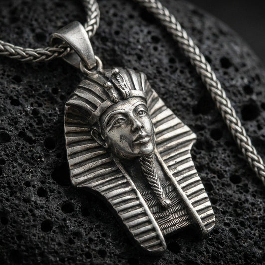 Sterling silver pharaoh head pendant with an oxidized finish, detailed Egyptian headdress and face relief, close-up on black volcanic rock