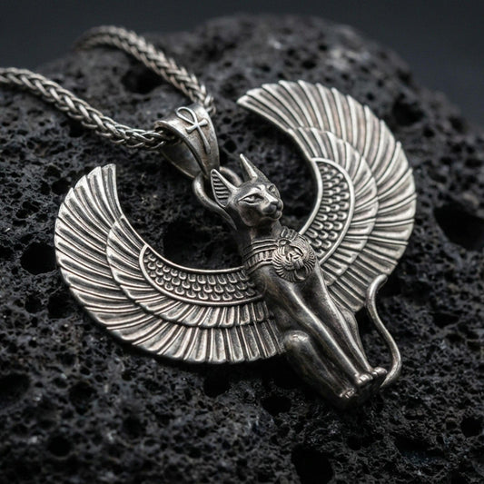 Sterling silver winged cat pendant inspired by Egyptian Bastet with an oxidized finish, detailed feather wings and feline body relief, close-up on black volcanic rock