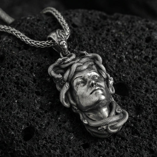 Oxidized Medusa head pendant necklace on textured volcanic rock, close-up centered composition with detailed snake relief and dramatic studio lighting.