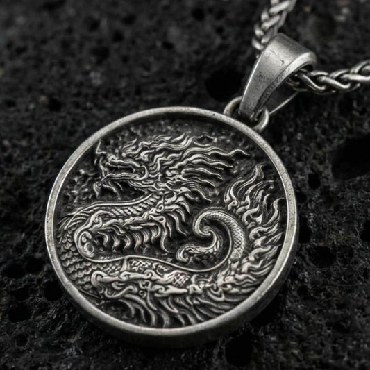 Oxidized round dragon coin pendant necklace on textured volcanic rock, centered close-up highlighting the engraved scales, flowing mane, and deep antique contrast.