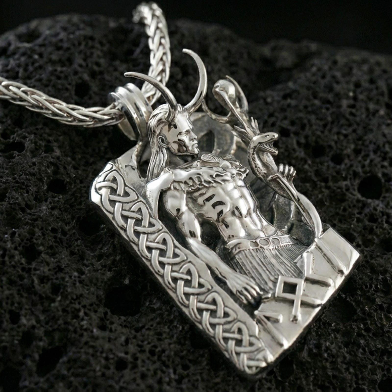 Polished silver Loki pendant necklace on textured volcanic rock, sharp macro product photo emphasizing the clean sculpted muscles, rune accents, and crisp edges.