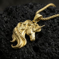 Load image into Gallery viewer, Gold plated unicorn head pendant necklace on textured volcanic rock, premium close-up with warm reflective shine across the horn and wavy hair contours.
