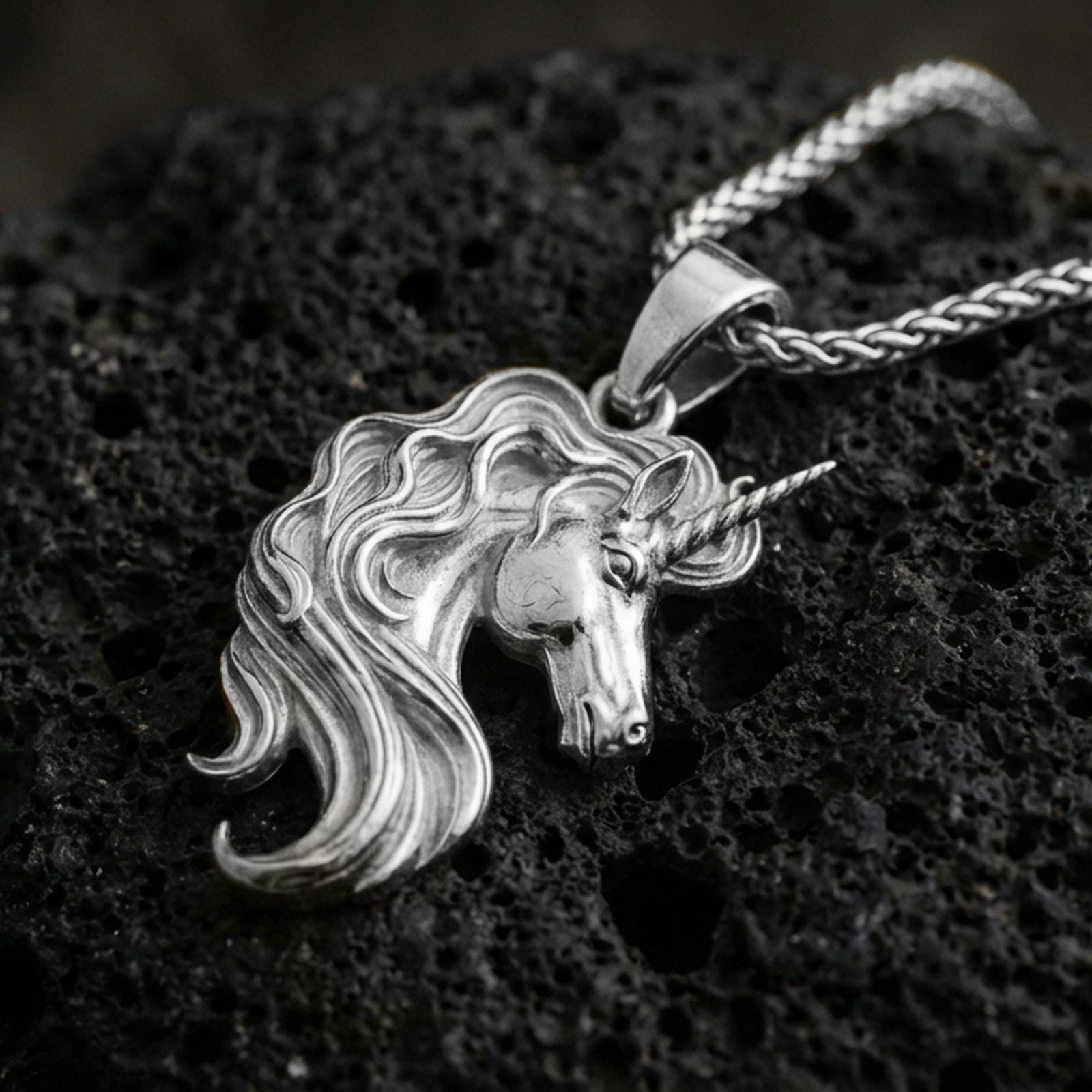 Polished silver unicorn head pendant necklace on textured volcanic rock, crisp macro product photo emphasizing bright reflections, clean edges, and sculpted mane detail.