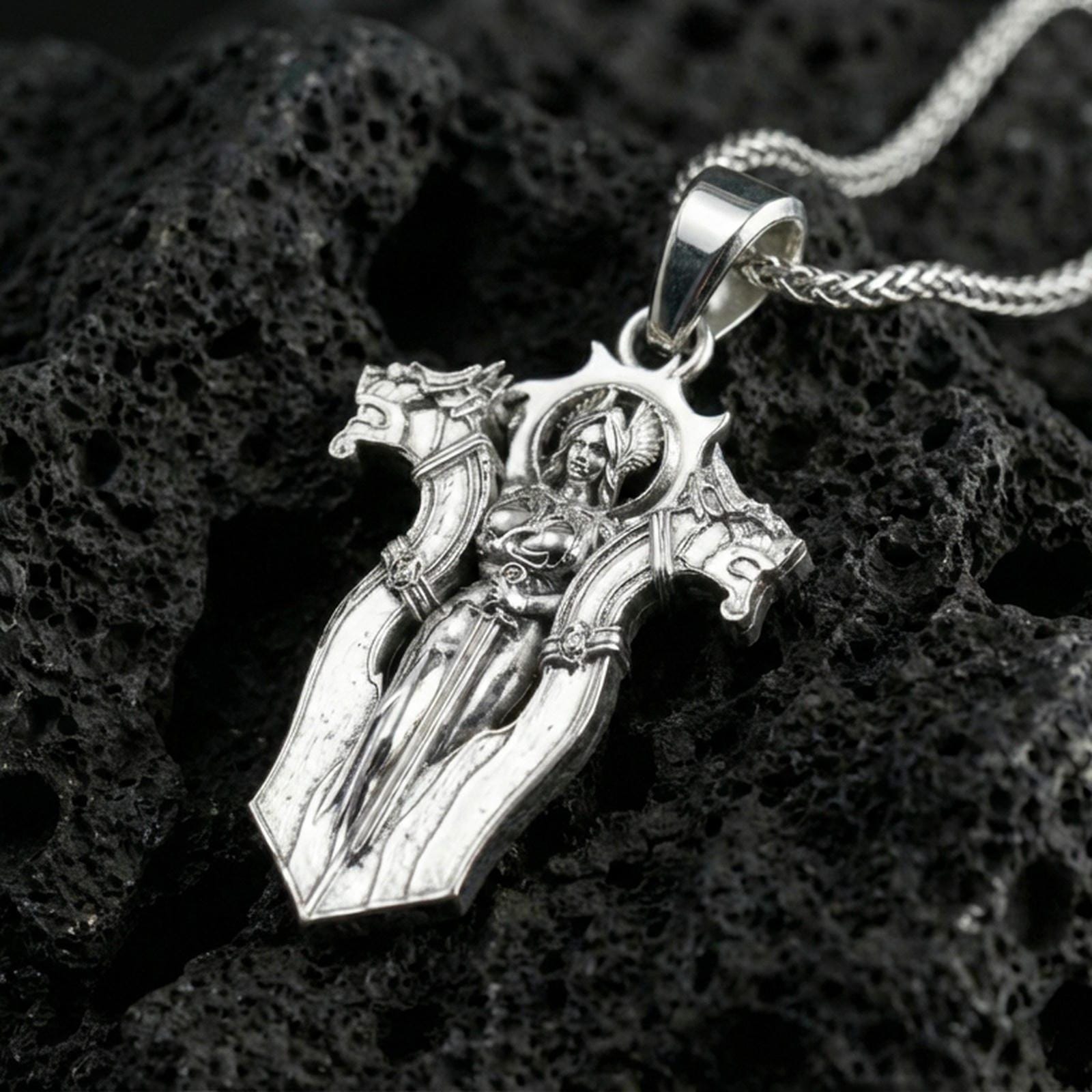 Polished silver gothic cross pendant necklace on textured volcanic rock, crisp macro product photo emphasizing clean reflections and the detailed warrior relief.