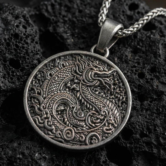 Oxidized dragon medallion pendant necklace on textured volcanic rock, centered close-up highlighting the coiled dragon, swirling cloud motifs, and deep antique shadowed contrast.