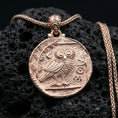 Load image into Gallery viewer, Rose gold plated owl coin pendant necklace on textured volcanic rock, centered studio-style close-up showcasing soft rosy glow and detailed owl-and-symbol engraving.

