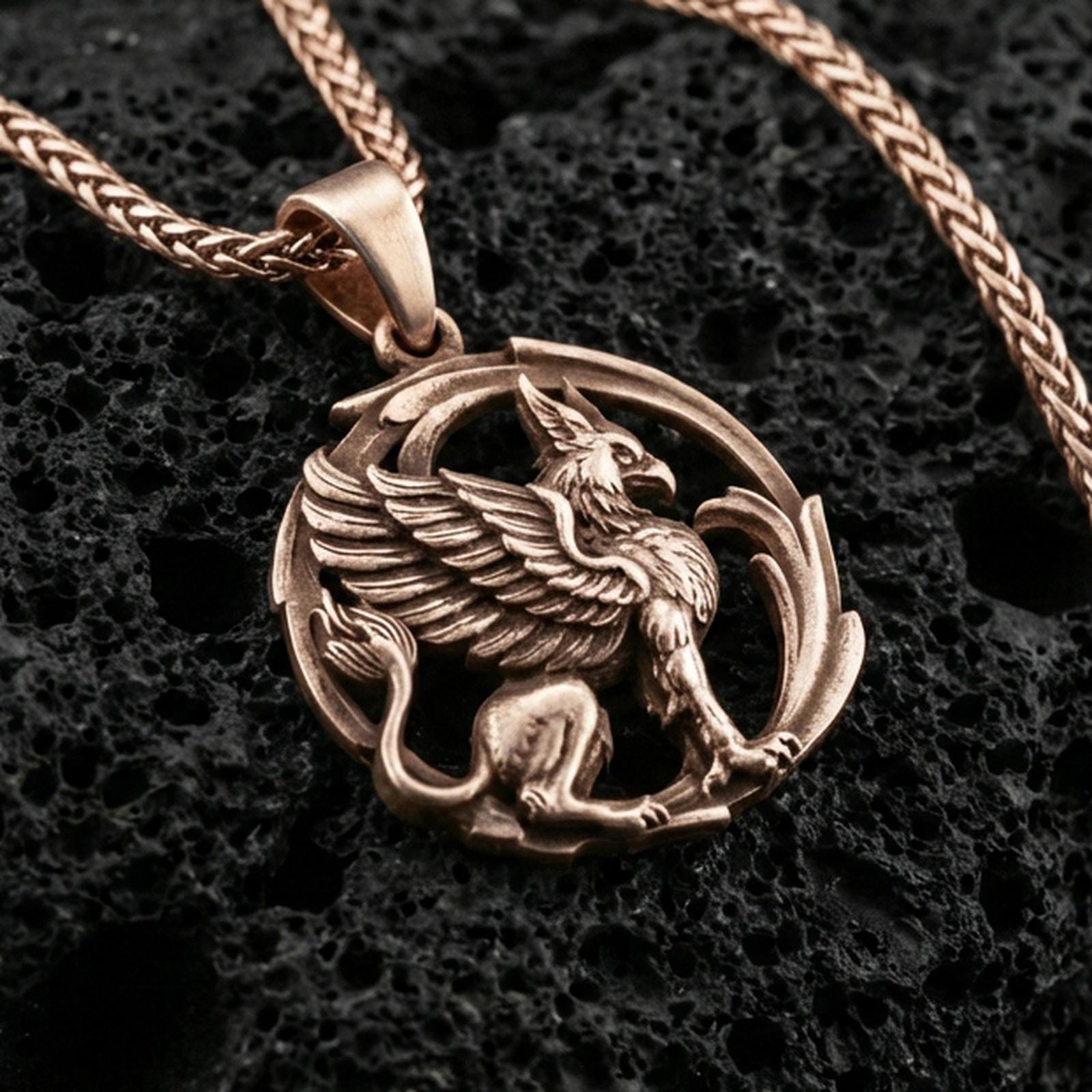 Rose gold plated griffin pendant necklace on textured volcanic rock, centered studio-style close-up showcasing soft rosy glow and intricate gryphon detailing throughout the design.