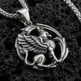 Load image into Gallery viewer, Oxidized griffin pendant necklace on textured volcanic rock, centered close-up highlighting the winged gryphon relief, curled tail, and deep antique shadowed contrast.
