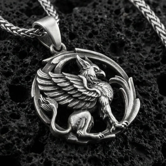 Oxidized griffin pendant necklace on textured volcanic rock, centered close-up highlighting the winged gryphon relief, curled tail, and deep antique shadowed contrast.