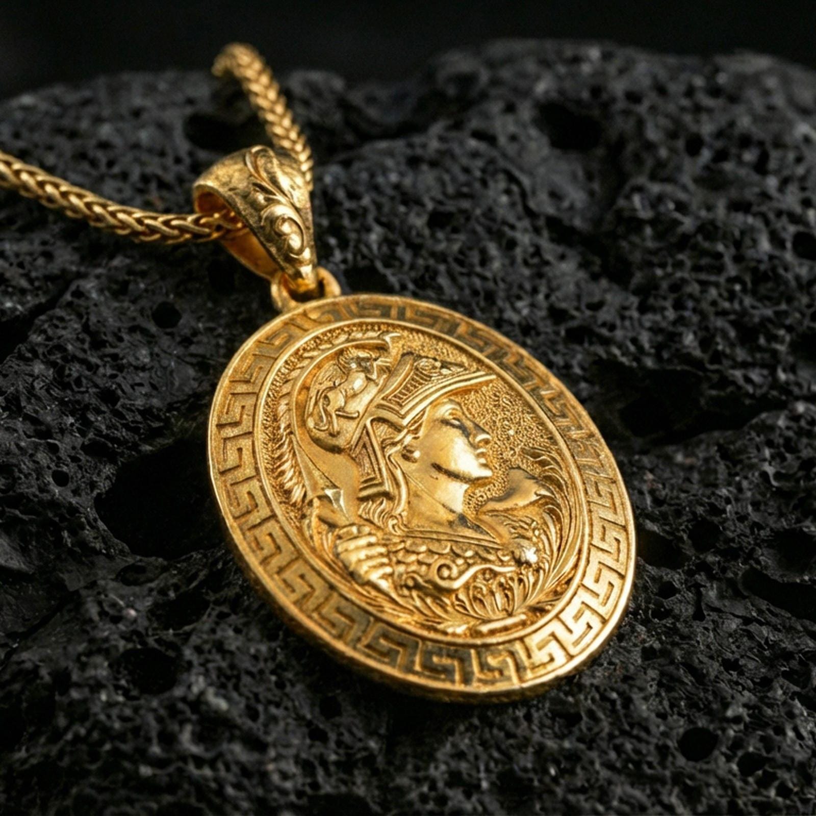 Gold plated Athena coin pendant necklace on textured volcanic rock, premium close-up with warm reflective shine across the helmet details, raised border, and Greek meander frame.