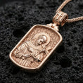 Load image into Gallery viewer, Rose gold plated Catholic saint pendant with Saint Francis figure, halo detail, and framed icon design resting on volcanic rock in an elegant close-up product presentation
