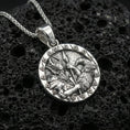 Load image into Gallery viewer, Polished silver Odin and raven medallion pendant necklace on textured volcanic rock, crisp macro product photo emphasizing clean edges, sharp feather engraving, and detailed Norse scene relief.
