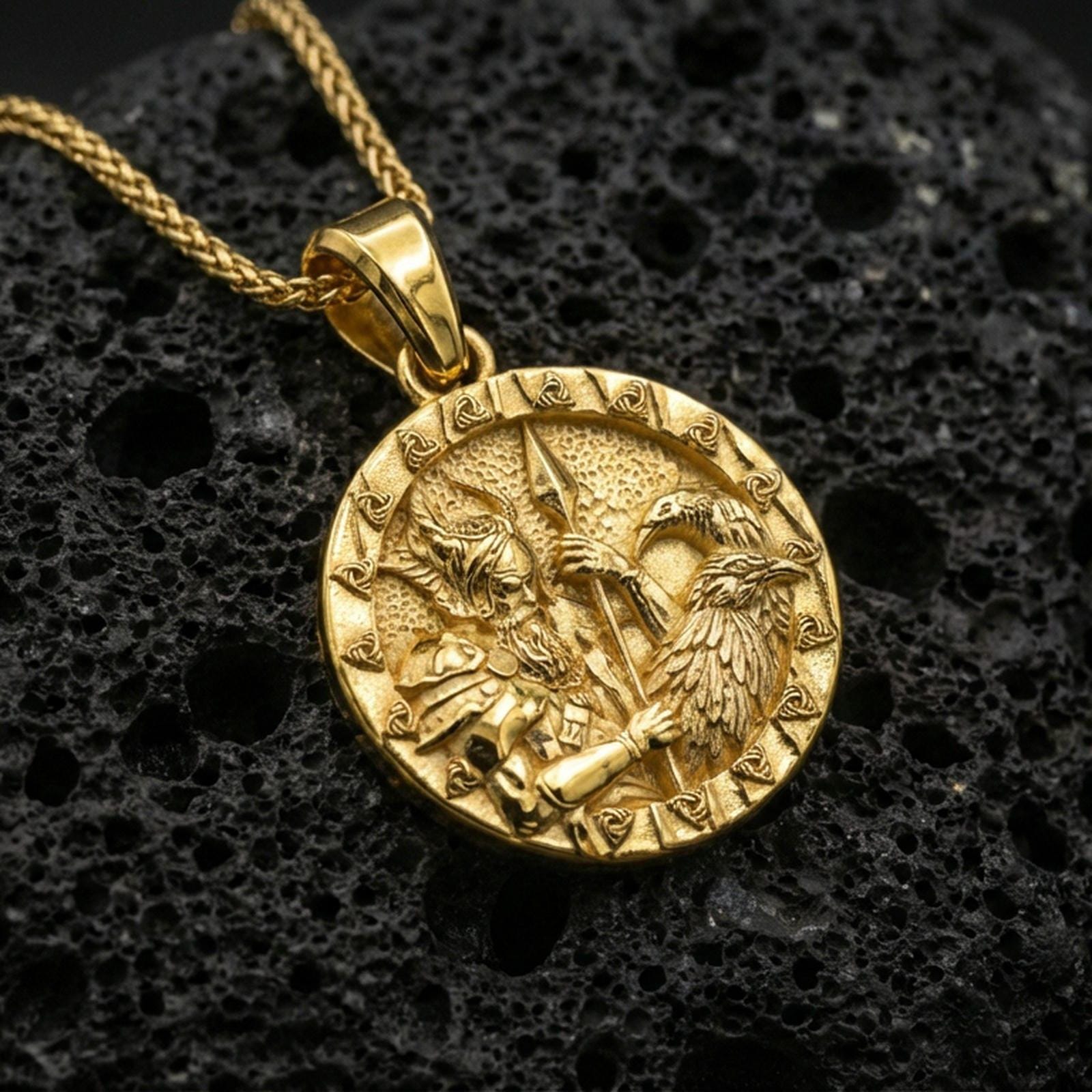 Gold plated Odin and raven medallion pendant necklace on textured volcanic rock, premium close-up with warm reflective shine across the warrior figure, raven wings, and raised border pattern.