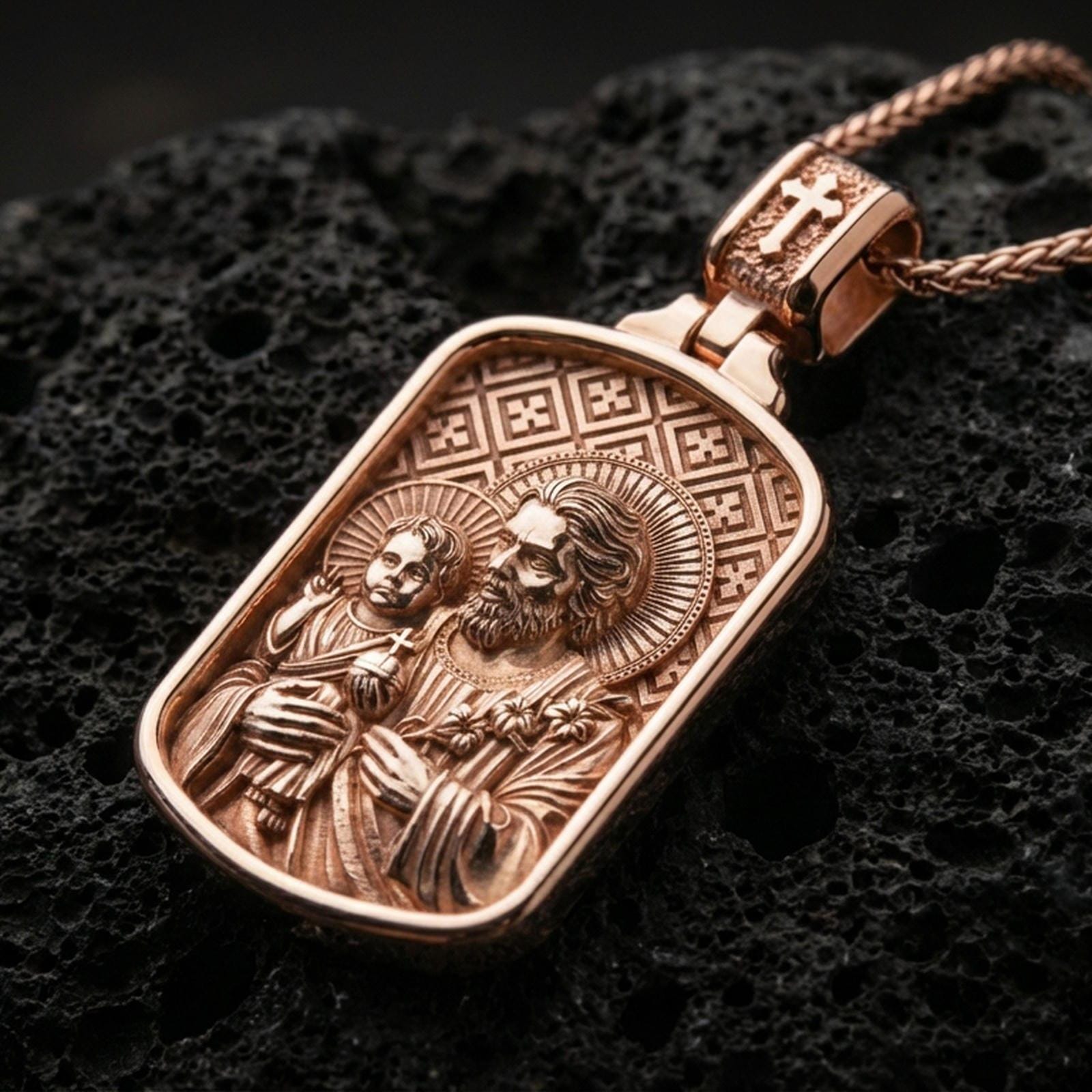 Rose gold plated Catholic Saint Joseph pendant with Child Jesus, halo accents, and framed icon design resting on volcanic rock in an elegant close-up product presentation