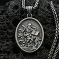Load image into Gallery viewer, Oxidized saint medallion pendant with a seated bearded figure, lion detail, and open scripture relief displayed on dark volcanic rock in a close-up luxury jewelry composition

