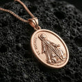 Load image into Gallery viewer, Rose gold plated religious Saint Rochus pendant with oval silhouette, halo detail, and dog companion resting on volcanic rock in an elegant close-up product presentation

