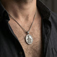 Load image into Gallery viewer, Oxidized Saint Rochus medallion with pilgrim staff and dog worn on the neck in a lifestyle jewelry shot, styled against the chest for a devotional and timeless look
