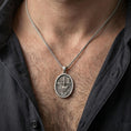 Load image into Gallery viewer, Oxidized resurrection medal pendant with risen Christ worn on the neck in a lifestyle jewelry shot, styled against the chest for a bold and devotional look
