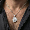 Load image into Gallery viewer, Polished silver religious Jesus pendant with resurrection relief and victory banner worn on the neck in a close lifestyle frame, highlighting the sacred symbolism and oval silhouette
