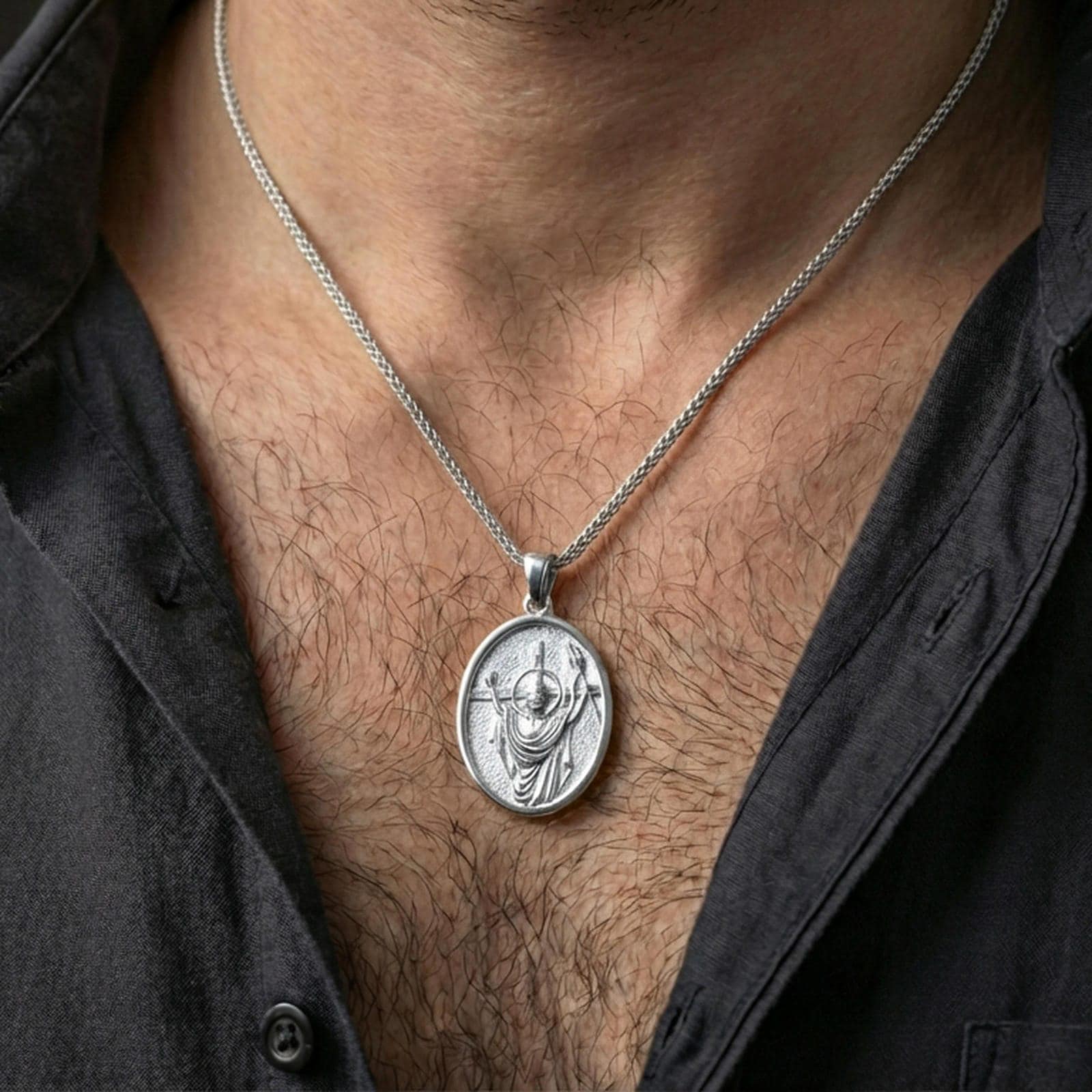 Polished silver religious Jesus pendant with resurrection relief and victory banner worn on the neck in a close lifestyle frame, highlighting the sacred symbolism and oval silhouette