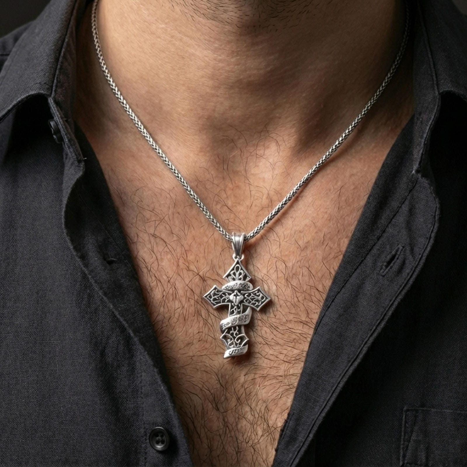 Polished silver Christian statement cross pendant with openwork detailing and engraved ribbon text worn on the neck in a close lifestyle frame, highlighting the decorative relief and message
