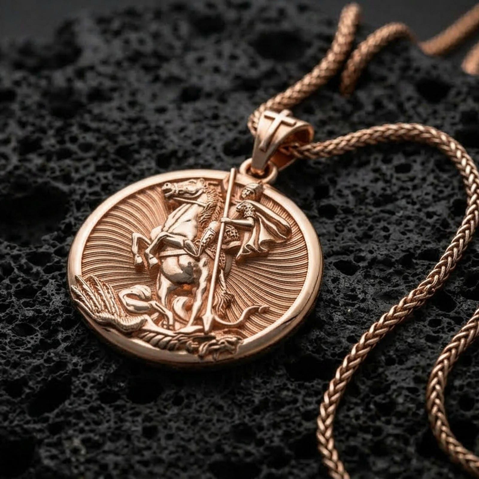 Rose gold plated Saint George pendant with horse rider relief, circular silhouette, and symbolic battle scene resting on volcanic rock in an elegant close-up product presentation